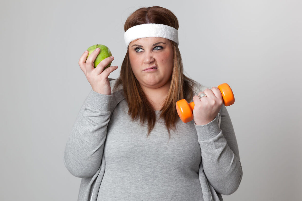 Annoyed woman holding and apple and a dumbbell.