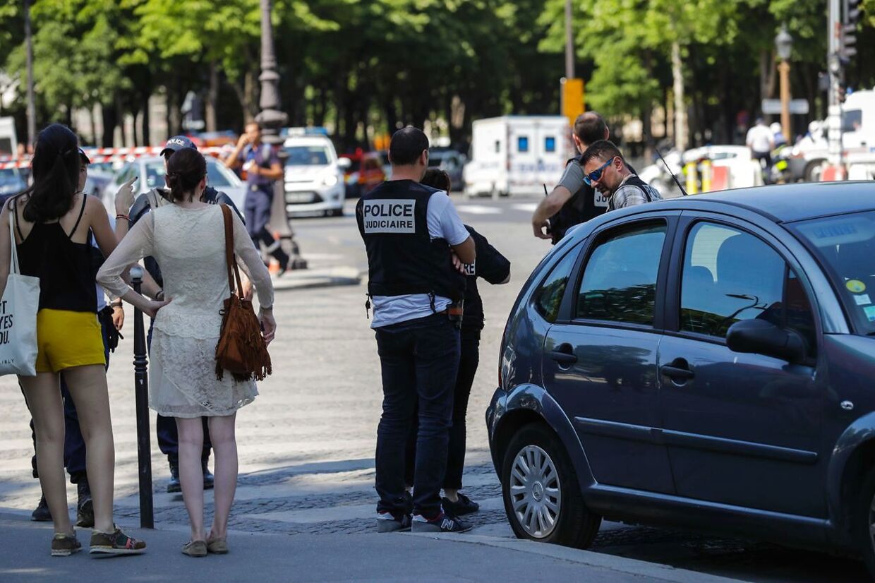 Police officers (C and R) and pedestrians (L) stand by a sealed off area on June 19, 2017 on the Champs-Elysees avenue in Paris, after a car crashed into a police van before bursting into flames, with the driver being armed, probe sources said. / AFP PHOTO / Thomas Samson