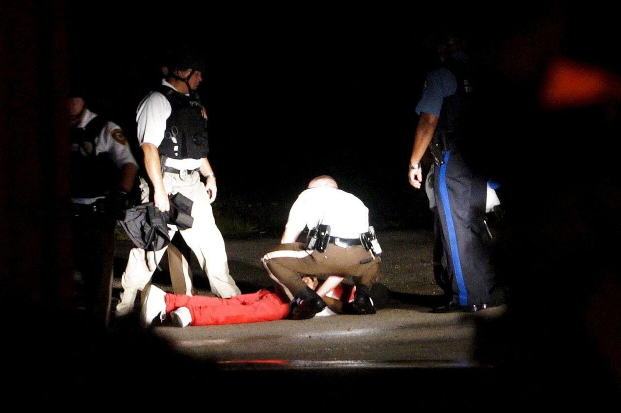 Politiet i Ferguson sidder ved en sort mand, der har blod på sin trøje. Det vides ikke, om manden 'kun' er såret eller er dræbt af skud.