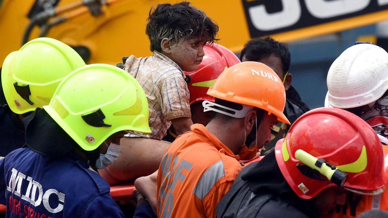 Redningsarbejdere bærer en fire-årig dreng ud fra murbrokkerne, efter han er blevet reddet ud af den kollapsede bygning.