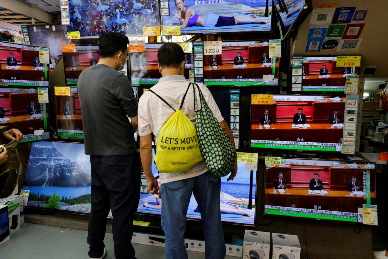 To forbipasserende ser her på tv-skærme i en butik i Hongkong, mens Den Nationale Folkekongres vedtager ændringer i Hongkongs valglov. Tyrone Siu/Reuters