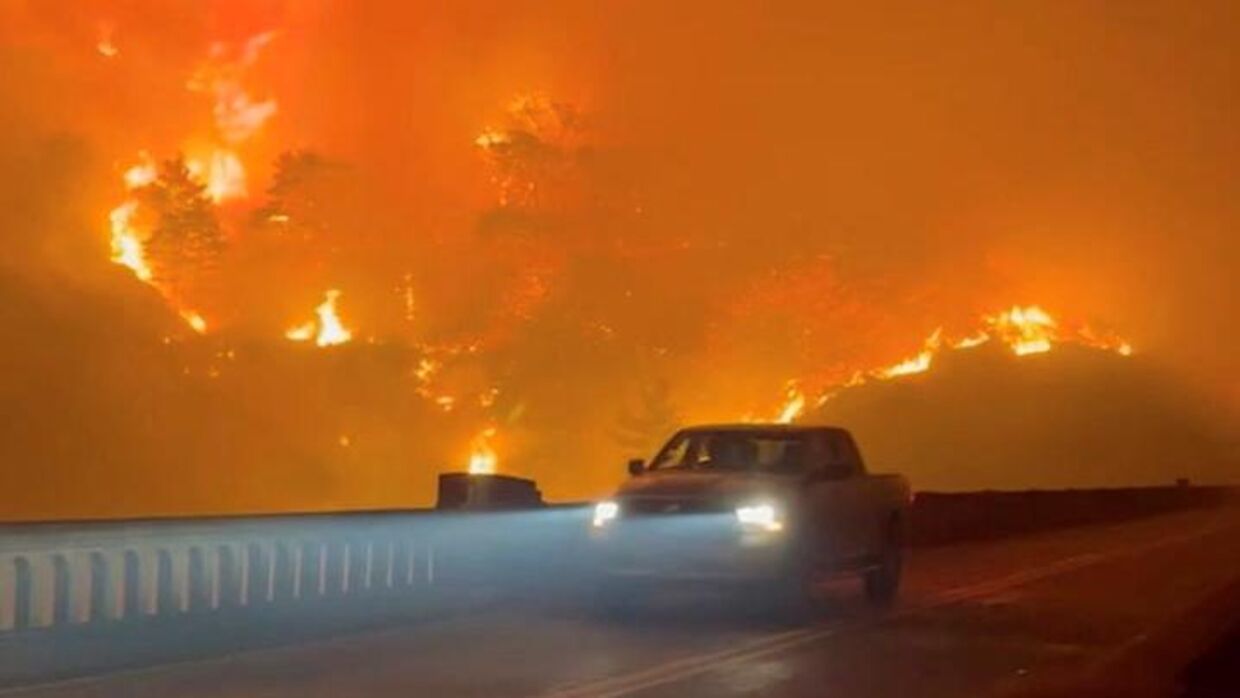 En bil kører over Rocky Creek Bridge ved Big Sur, der er oplyst af flammerne.
