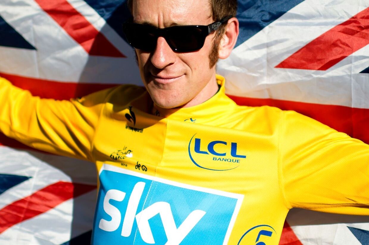 (FILES) This file photo taken on July 22, 2012 shows overall leader's yellow jersey, British Bradley Wiggins, wrapped in a national flag, celebrates during his parade at the end of the 120 km and last stage of the 2012 Tour de France cycling race starting in Rambouillet and finishing in the famous Paris-Champs-Elysees Avenue, on July 22, 2012. Bradley Wiggins announced his retirement from professional cycling on December 28, 2016, bringing the curtain down on a career that saw him become one of Britain's greatest sportsmen. The 36-year-old became Britain's first Tour de France winner in 2012 and bows out with eight Olympic medals, including five golds, and seven world titles, across track and road cycling, to his name. / AFP PHOTO / JEFF PACHOUD