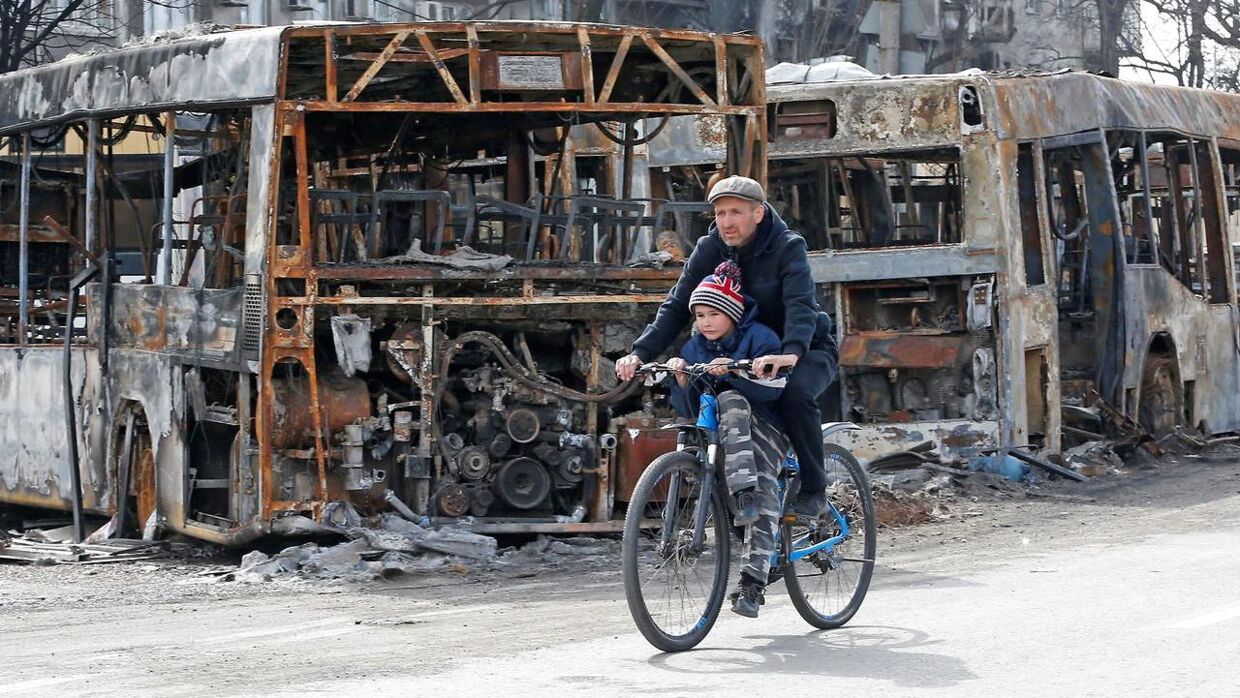 A man and a child ride a bicycle past burnt out buses during Ukraine-Russia conflict in the southern port city of Mariupol, Ukraine April 19, 2022. REUTERS/Alexander Ermochenko