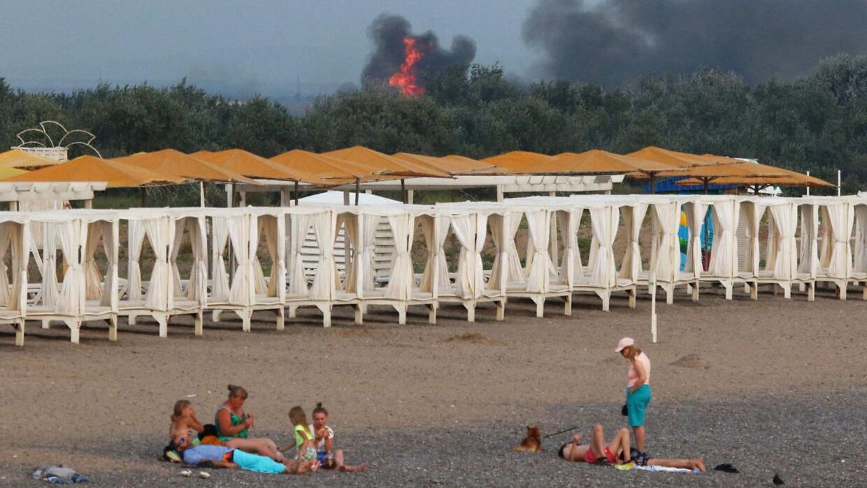 En gruppe mennesker på stranden ved Novofedorivka med en eksplosion i baggrunden.