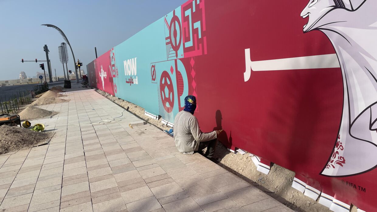 En migrantarbejder i fuld gang med at sætte reklamer op for den kommende VM-slutrunde midt på dagen i Doha.