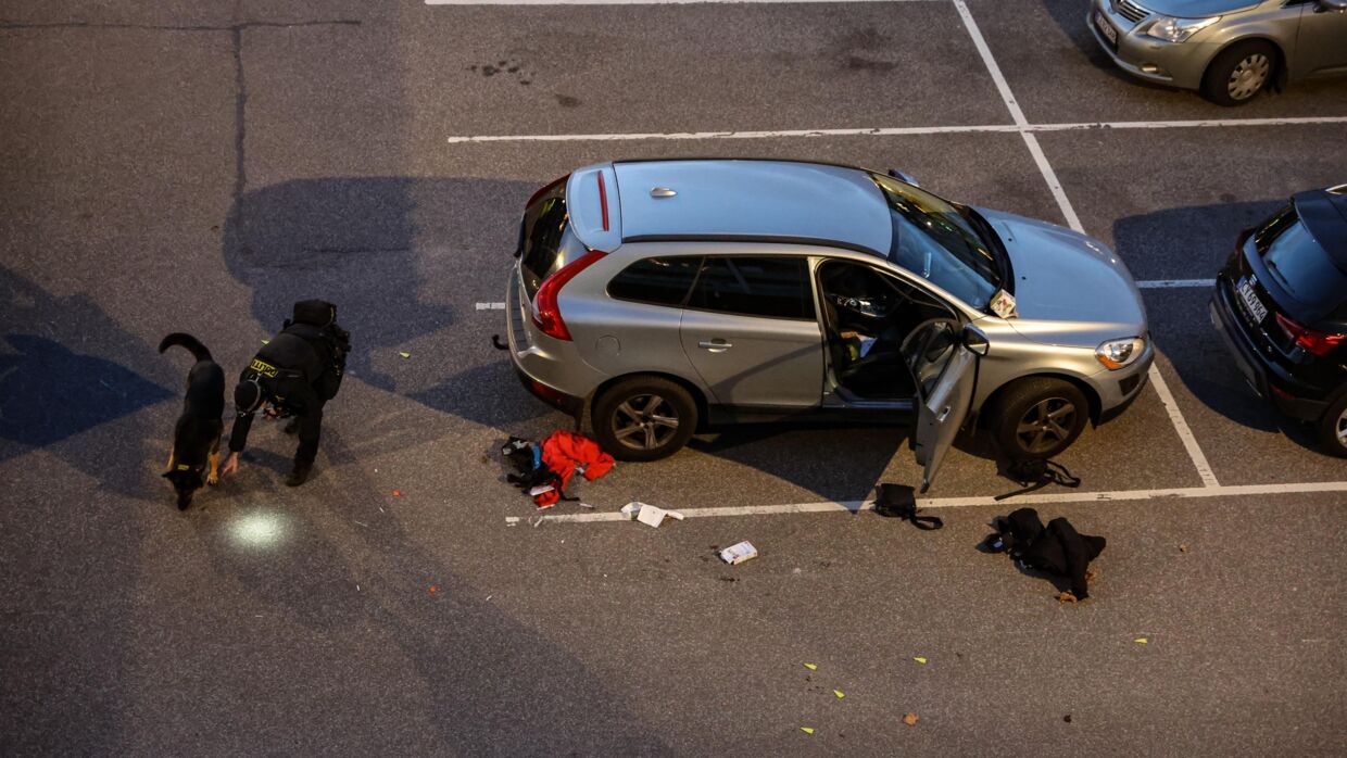 Den dræbte blev ramt af skud foran denne sølvgrå Volvo. Her ses politiet arbejde ved gerningsstedet, hvor der ligger en McDonald's Happy Meal i forruden.