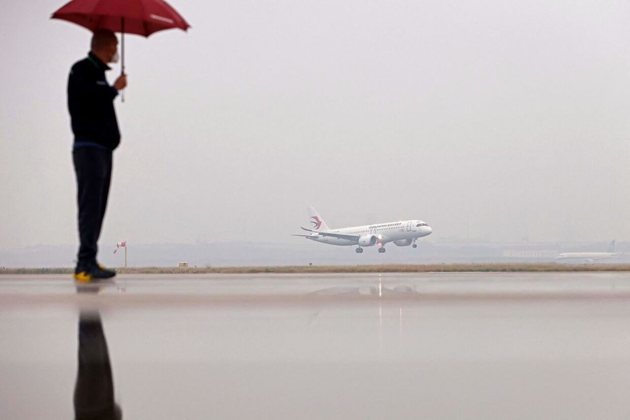 En mand med en paraply ser på, mens det nye kinesiske fly B919 lander i Hongqiao International Airport i Shanghai. Det er nu China Eastern Airlines ejendom.
