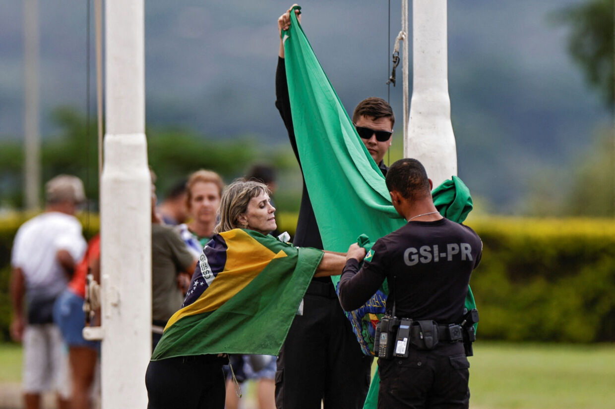 En Bolsonaro-tilhænger rækker ud for at røre ved det præsidentielle flag, som to sikkerhedsvagter har nedtaget uden for præsidentpaladset i hovedstaden Brasilia fredag. Ueslei Marcelino/Reuters