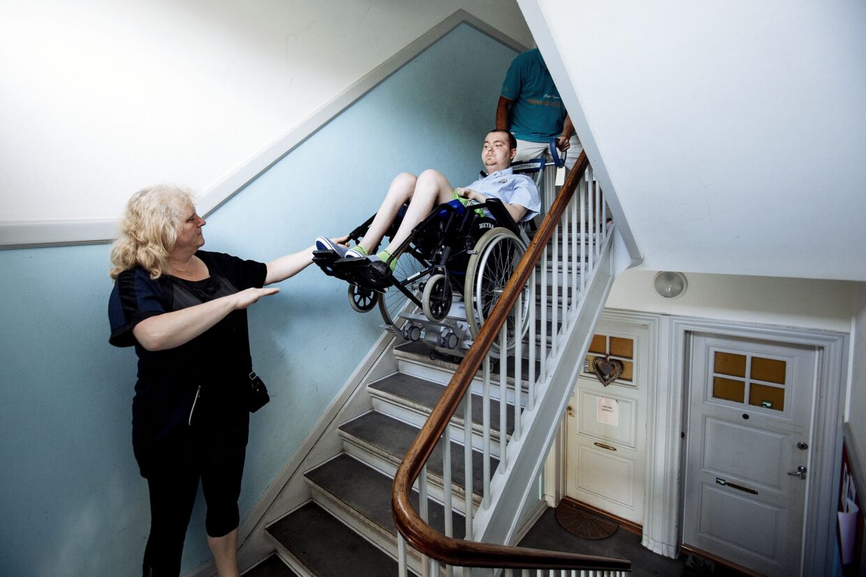Patrick Lehnert boede med sin mor og far i en lille lejlighed på Nørrebro i København. Da han blev lam fra livet og ned og derfor måtte sidde i kørestol, gjorde det turene til Rigshospitalet en noget mere omstændelige. Her hjælper hans mor Susann Lehnert med at få ham ned ad trappen.