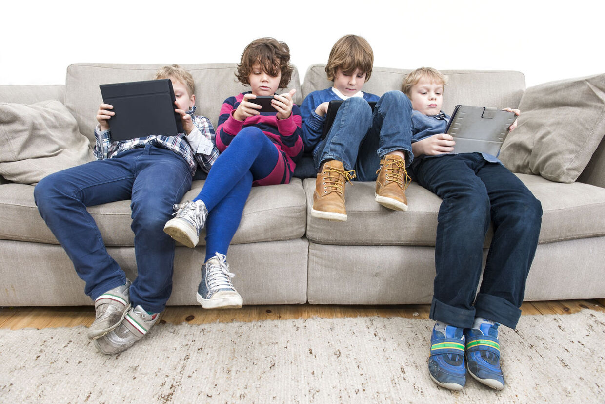 Brothers and sister using electronic devices while slouching on sofa at home